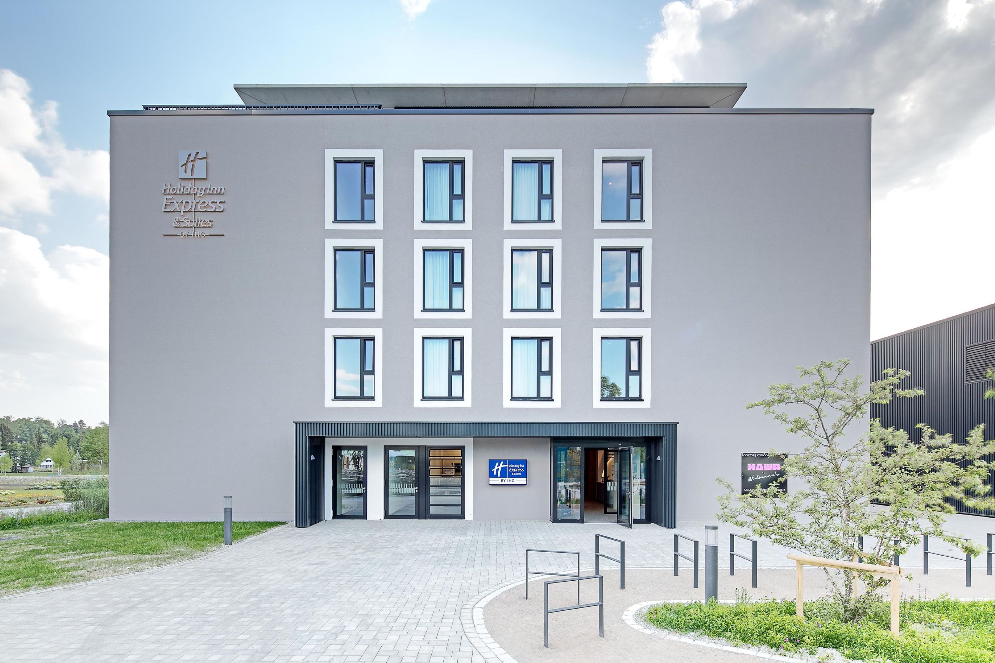 Een modern gebouw met een platte gevel, meerdere ramen en een bord waarop staat dat het een Holiday Inn Express & Suites is.