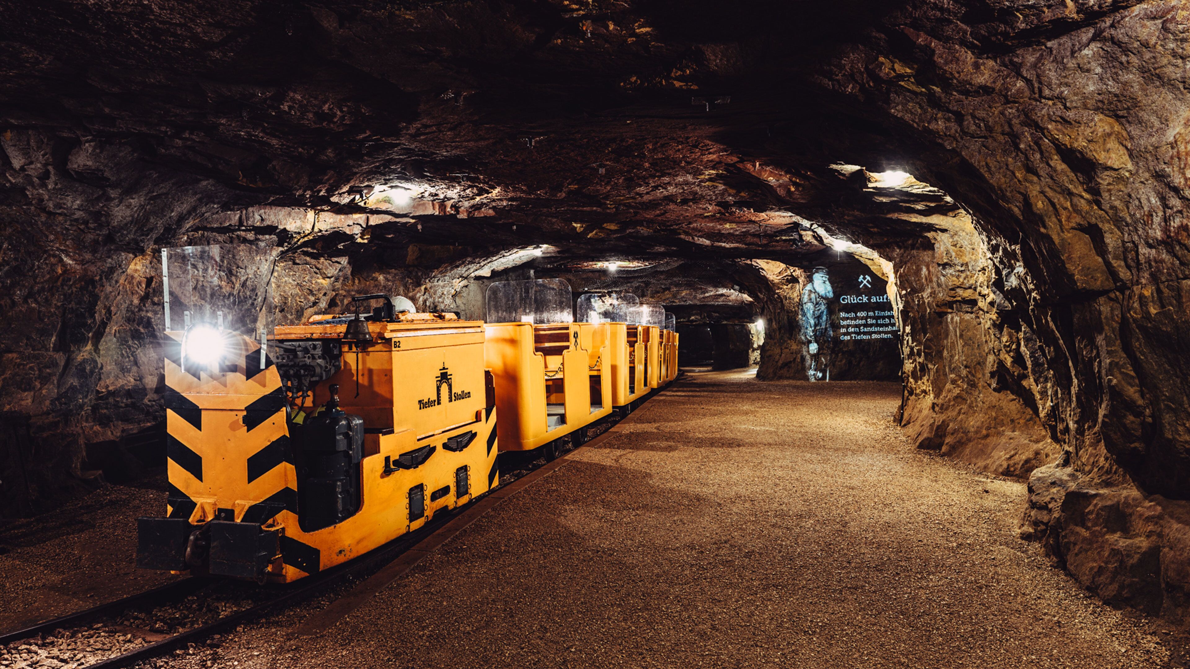A train in a tunnel with rocky walls and a sign in the distance.