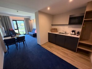 A modern hotel room with a kitchenette, a dining area with a table and chairs, a sofa, and a view through a large window. - Holiday Inn Express & Suites Ellwangen by IHG (Ellwangen)