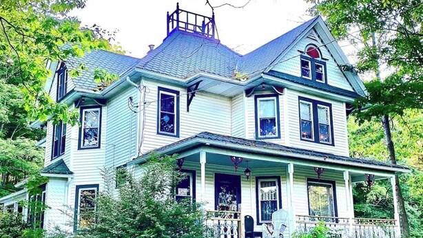 Une grande maison à deux étages, dotée d’un porche et d’une cheminée.