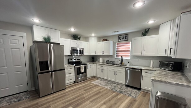 A modern kitchen with white cabinets, stainless steel appliances, and a wooden floor.