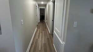 A narrow hallway with wooden flooring and white walls, leading to a door at the end.