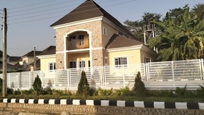 A two-story house with a stone facade, a balcony, and a fenced yard. - Dazzle Hotel and Apartment (Abuja)