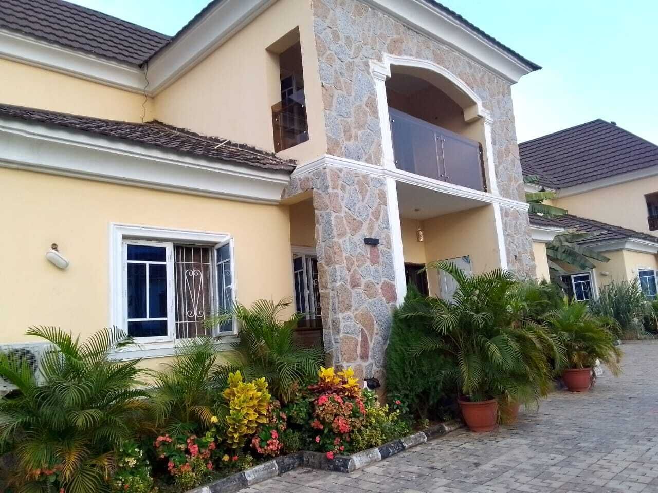 A two-story house with a stone pillar, a balcony, and a paved driveway.