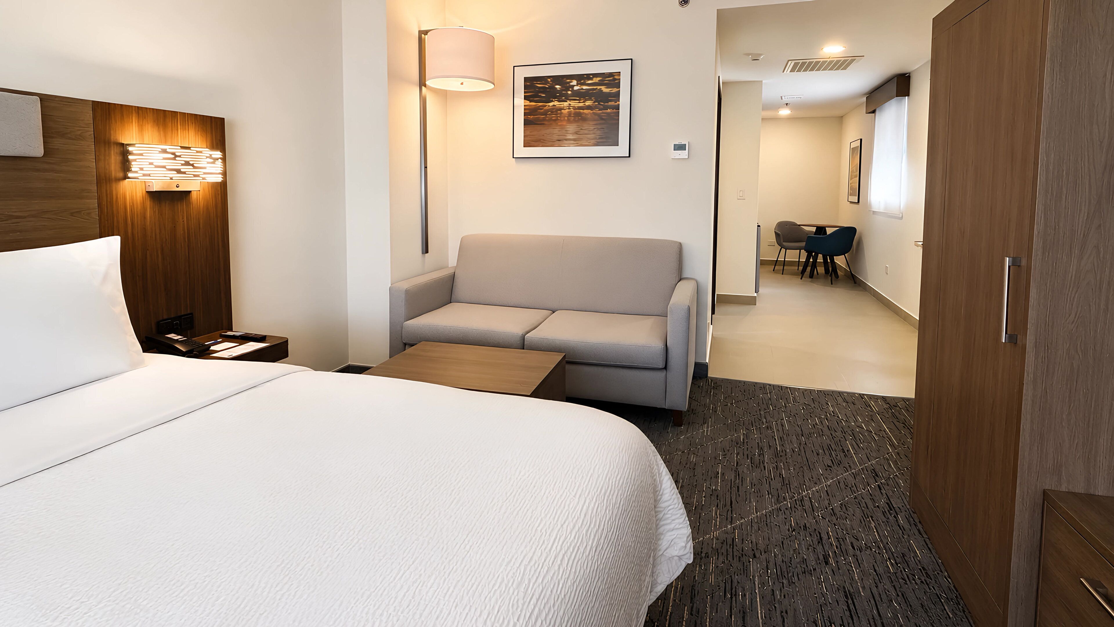 A hotel room with a bed, a sofa, a table, a lamp, and a picture on the wall.