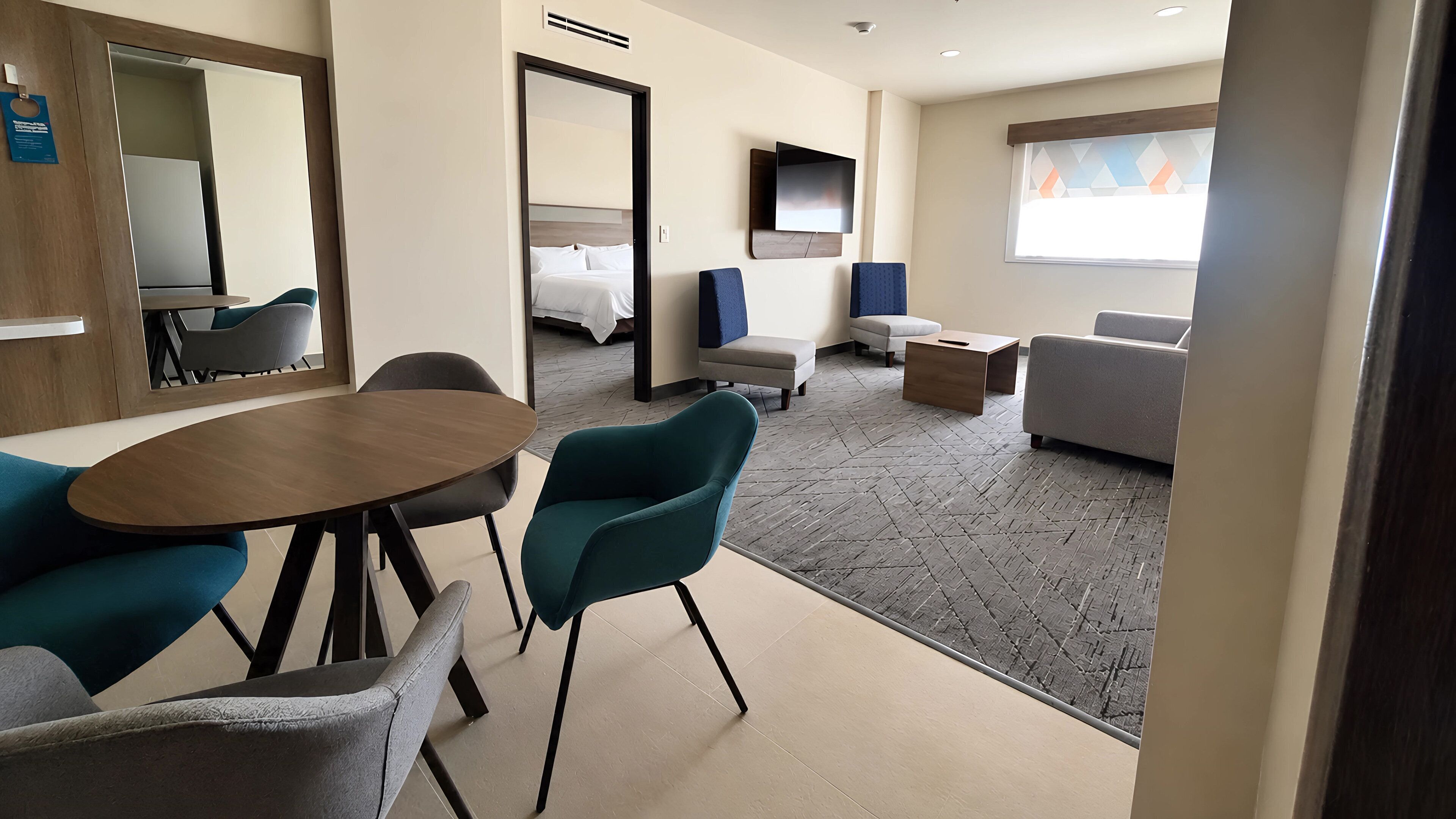 A hotel room with a dining area, a sofa, a TV, and a bed.