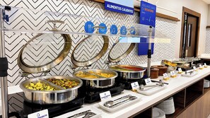 Un buffet proposant différents stands de nourriture, notamment un stand de pâtes et un stand de fruits, chacun étant clairement identifié par une signalétique.
