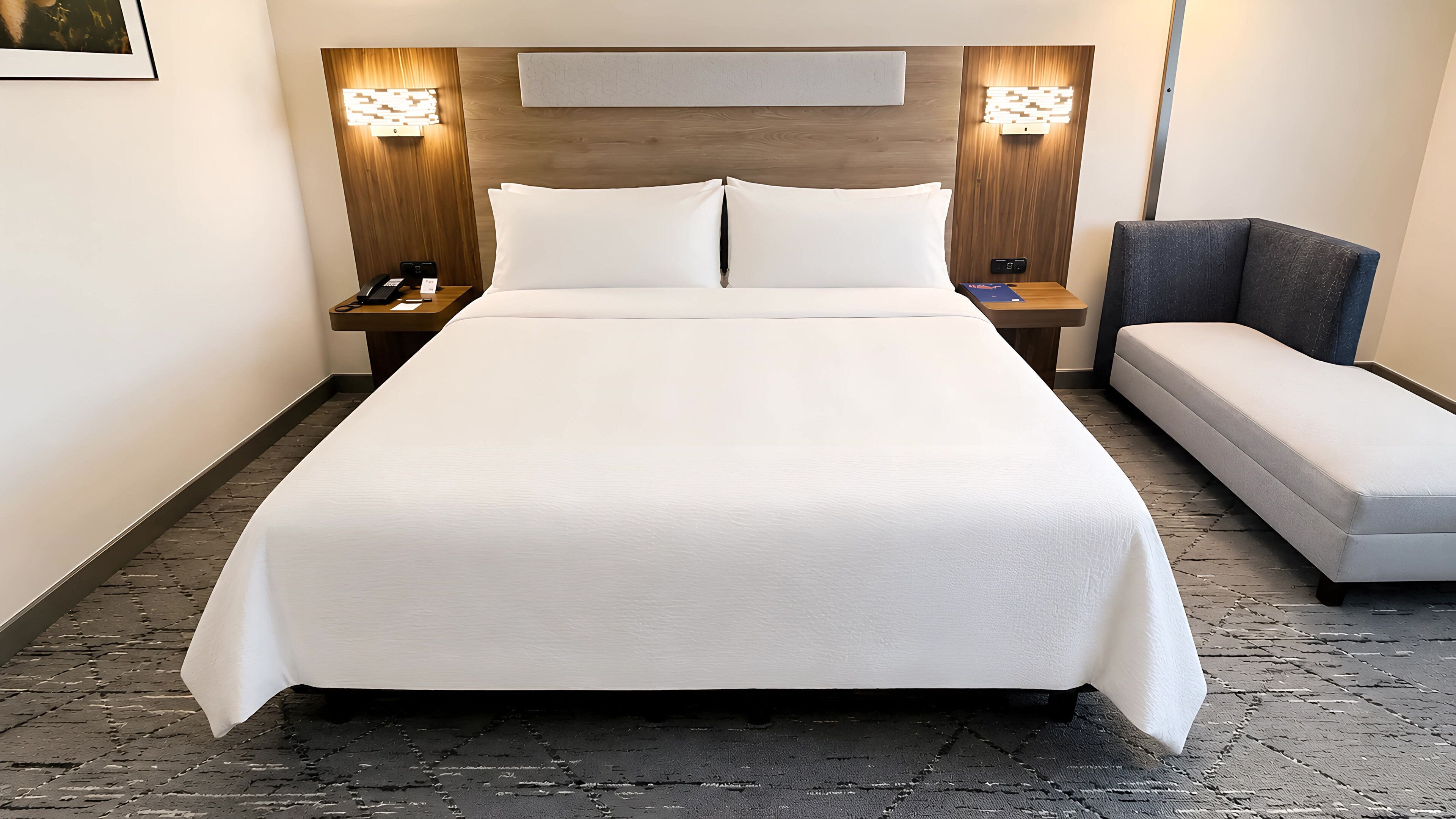 Una habitación de hotel con una cama grande, mesitas de noche con lámparas, un pupitre y un sofá.