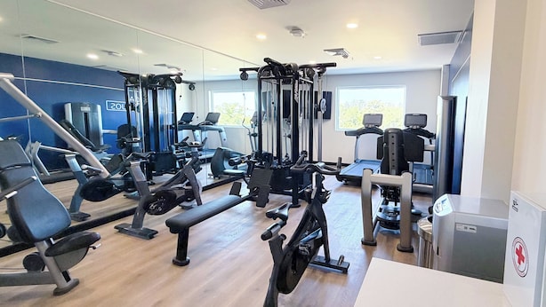 Ein Fitnessraum mit unterschiedlichen Trainingsgeräten, einer Bank und einer Spiegelwand.