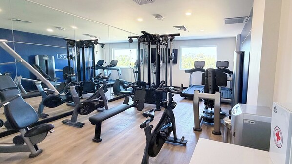 Ein Fitnessraum mit unterschiedlichen Trainingsgeräten, einer Bank und einer Spiegelwand.
