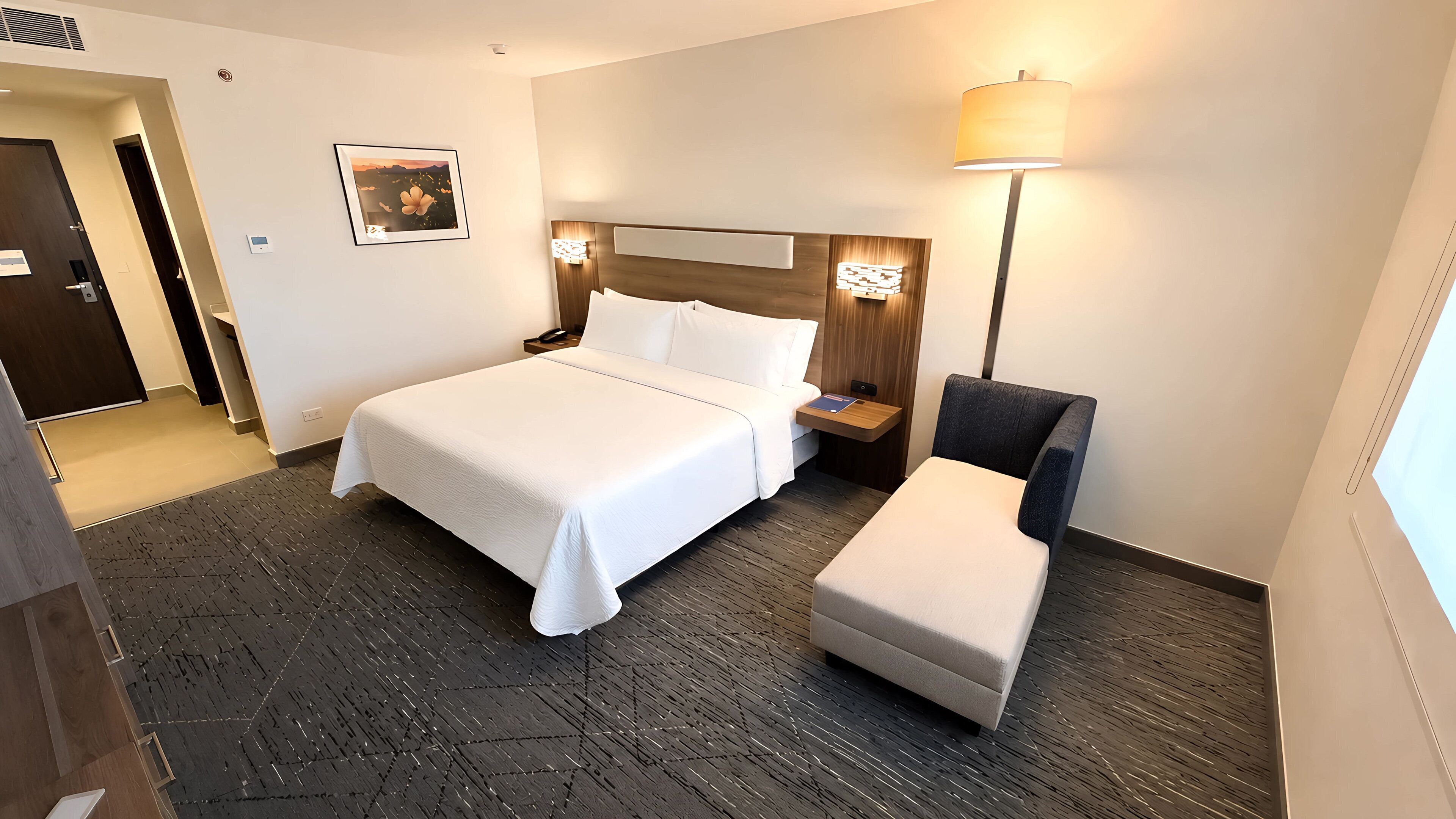 A hotel room with a large bed, a bedside table, a chair, a lamp, and a picture on the wall.