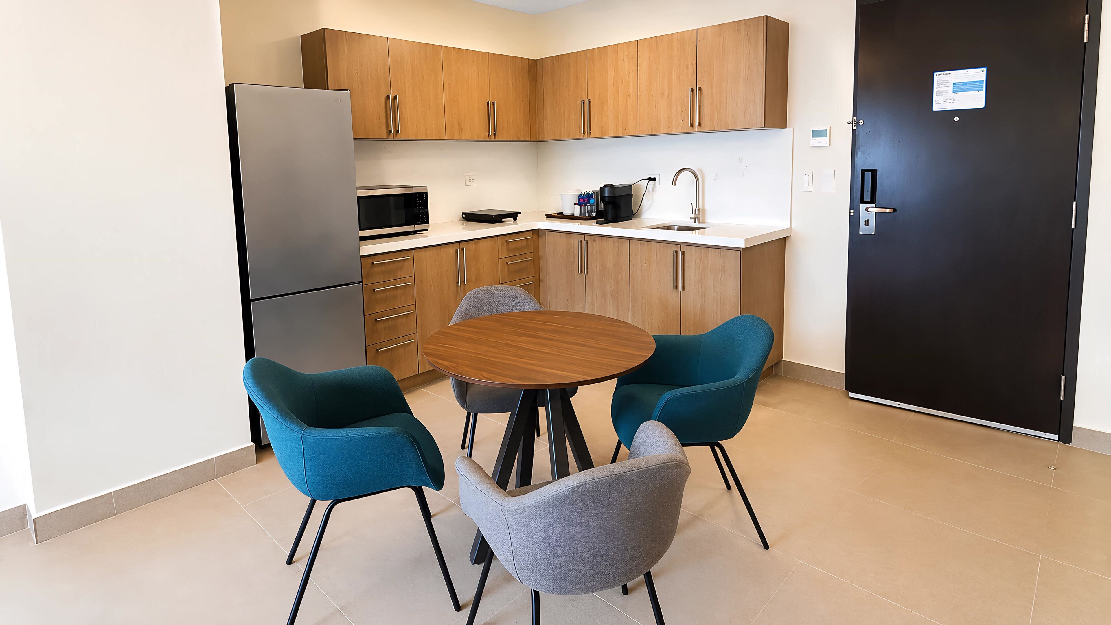 A modern kitchen with wooden cabinets, a black refrigerator, a microwave, a coffee maker, and a sink. There is a round table with four chairs.