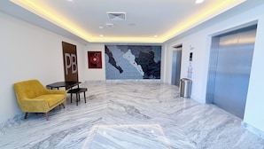 Eine Lobby mit Marmorboden, einem gelben Sessel, einem Tisch, einer Wand mit einer Karte und einem Aufzug.
