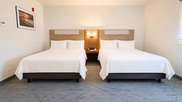 A hotel room with two beds, a nightstand, a wall-mounted light, and a framed picture.