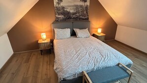 Un dormitorio con una cama, dos mesitas de noche, una lámpara colgante y un cuadro en la pared.