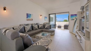 A modern living room with a sectional sofa, a glass coffee table, and a view of the sea through large windows. - Sea Side Apartment, 2 minutes' walk from the beach (Cap Malheureux)