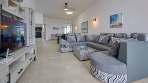 A modern living room with a sectional sofa, a flat-screen TV, and a dining area in the background. - Sea Side Apartment, 2 minutes' walk from the beach (Cap Malheureux)
