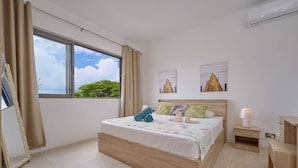 A bedroom with a large bed, a bedside table, a nightstand, a mirror, and a window with curtains. - Sea Side Apartment, 2 minutes' walk from the beach (Cap Malheureux)