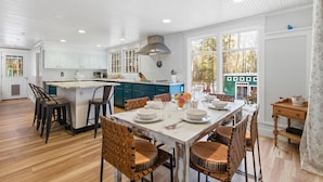 A spacious kitchen with a central island, wooden flooring, and large windows offering a view of the outside.
