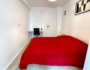 A bedroom with a red bedspread, a desk with a chair, and a door. - Bright 1 Bedroom near République Paris 10th (Paris)