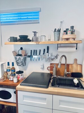 Une cuisine avec un plan de travail noir, un évier et un four à micro-ondes. Des étagères situées au-dessus servent à ranger les ustensiles de cuisine et les bocaux.