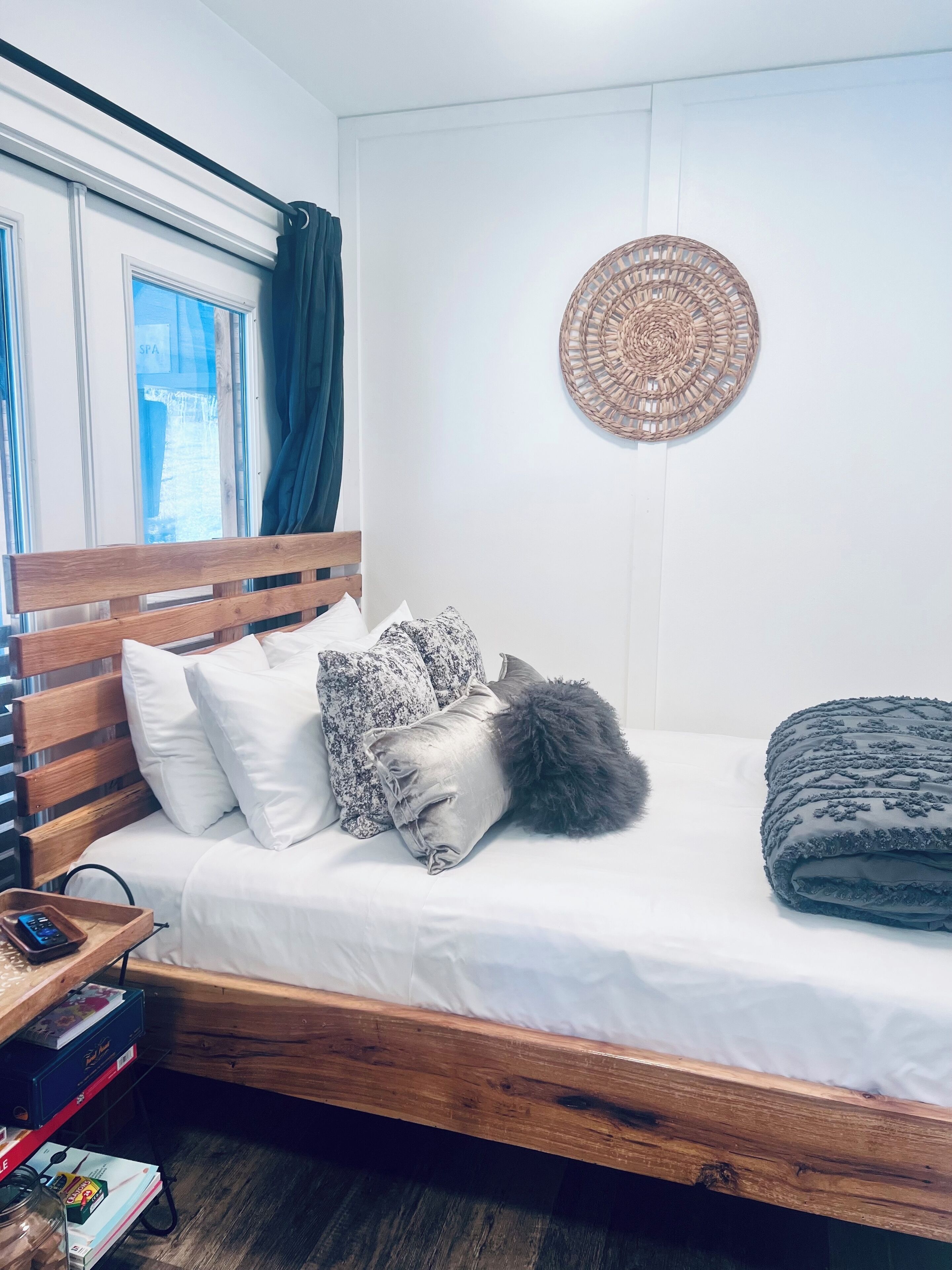 A bedroom with a wooden bed, white bedding, and a woven wall hanging.