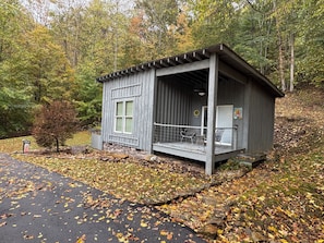 A rustic cabin with a porch, surrounded by autumn foliage.