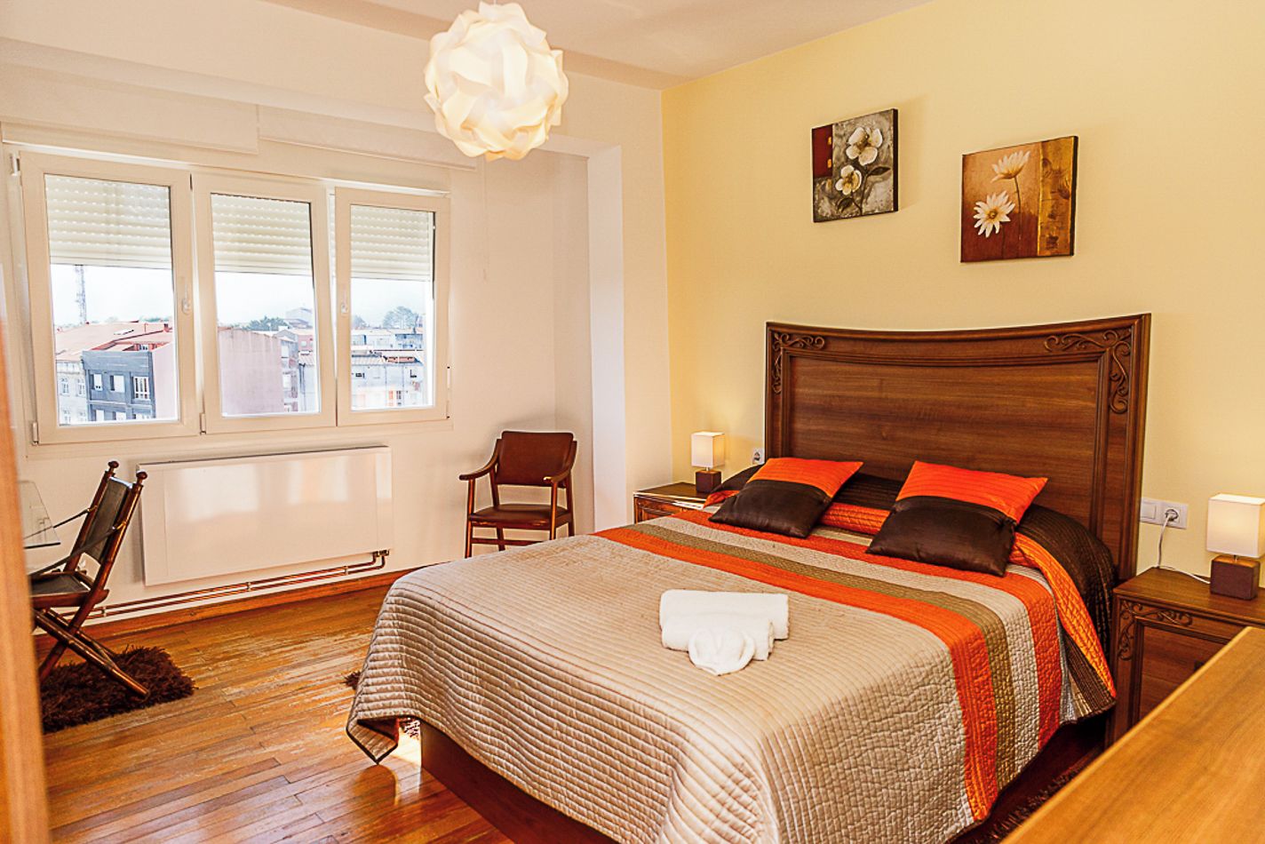 Habitación de hotel con una cama grande, cabecera de madera, una silla, ventana con persianas y una obra de arte en la pared.