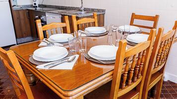Een eettafel gedekt voor zes personen, met houten stoelen, en een keuken in de achtergrond met een betegelde spatwand.