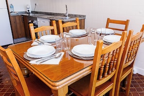 Une table à manger dressée pour six personnes, avec des chaises en bois, une cuisine en arrière-plan et un mur recouvert de carreaux.
