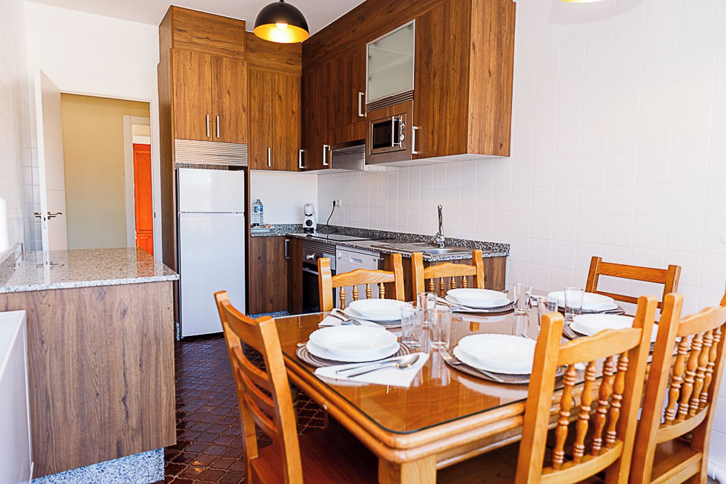 A compact kitchen with wooden cabinets, a built-in oven, and a dining table set for four.