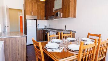 A compact kitchen with wooden cabinets, a built-in oven, and a dining table set for four.