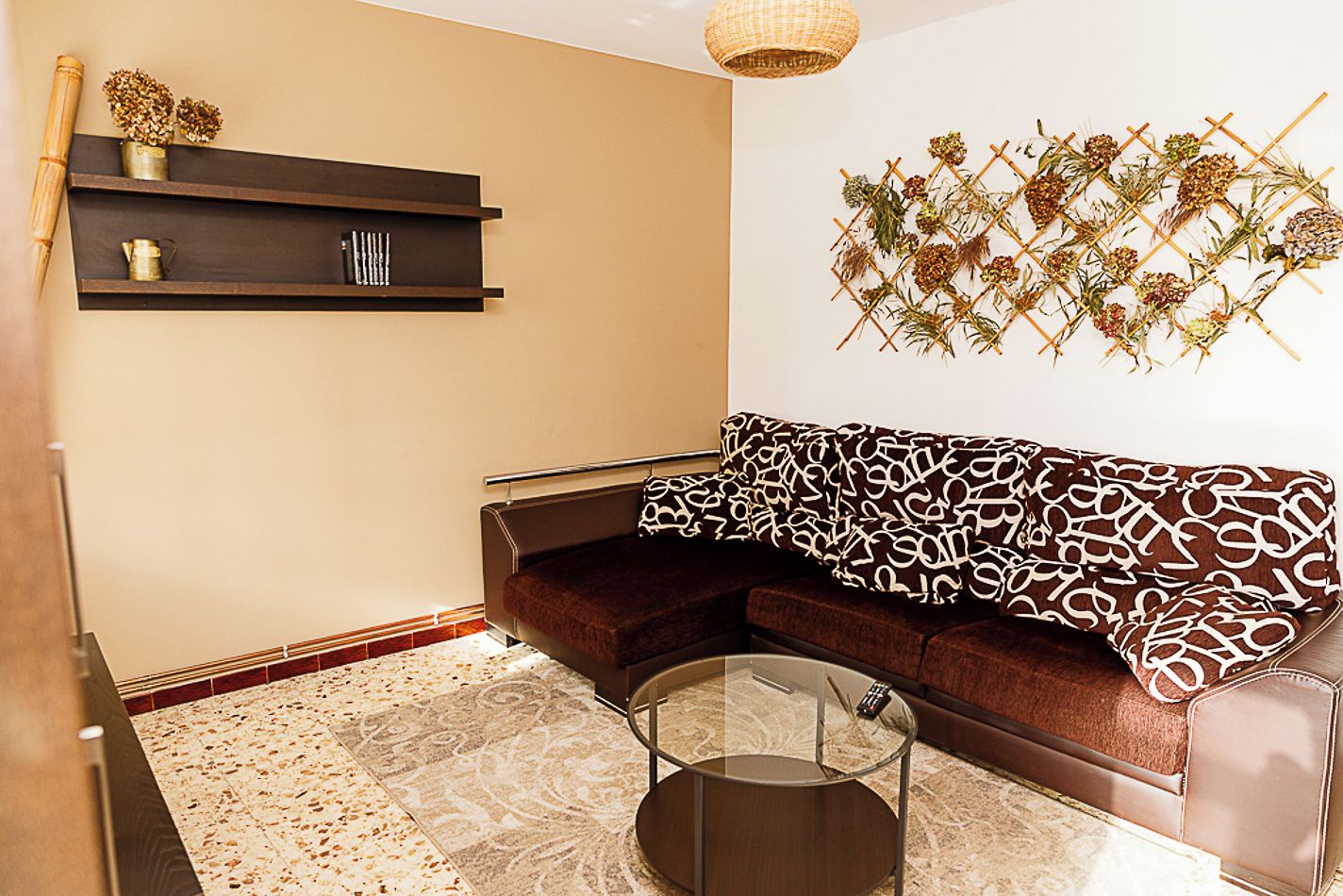 Een moderne woonkamer met een bruine bank, een glazen salontafel en een wandplank met decoratieve objecten.