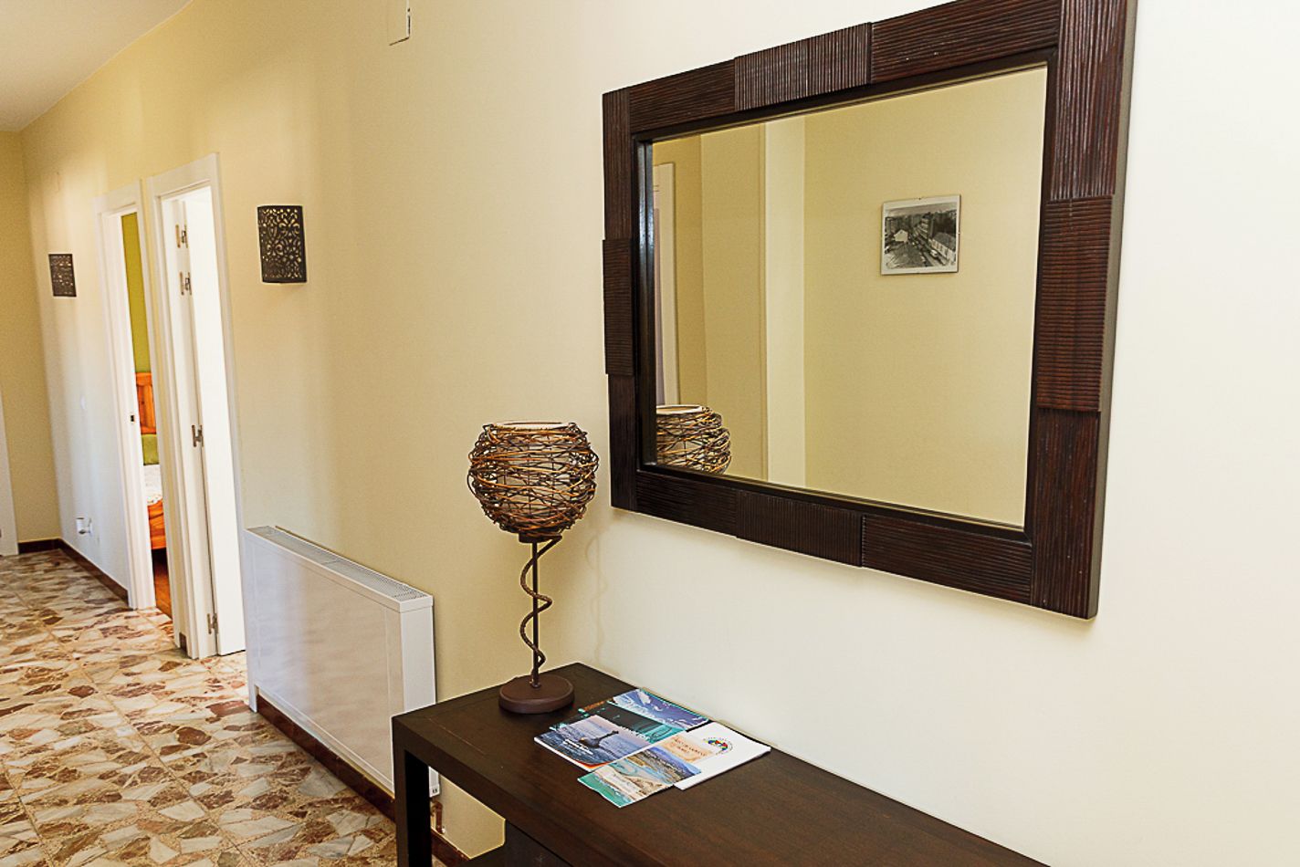 Un pasillo con un radiador, un espejo montado en la pared y una lámpara decorativa.