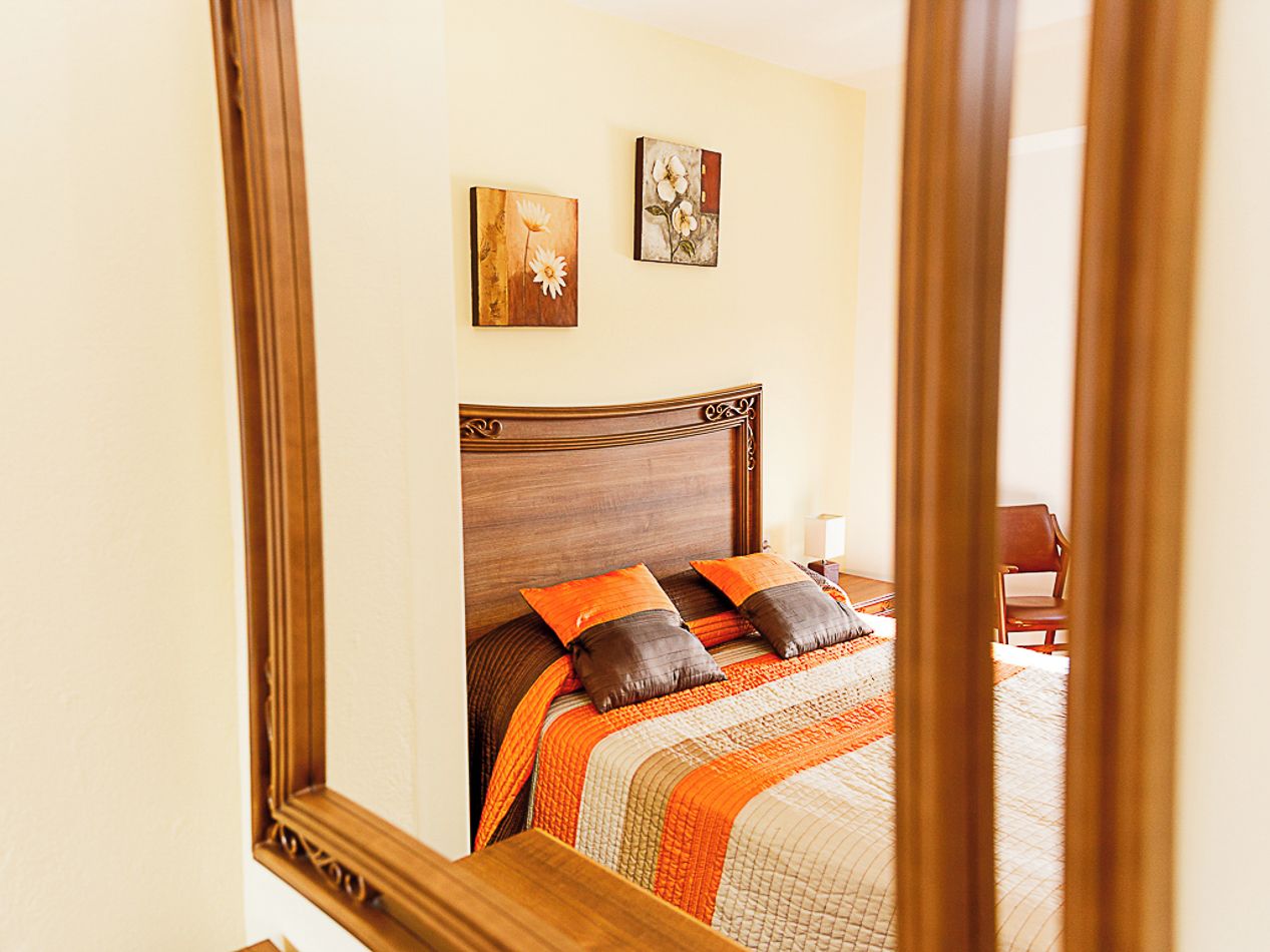Een slaapkamer met een houten hoofdeinde, een bed met okerkleurige en bruine beddengoed, en twee aan de muur bevestigde schilderijen.