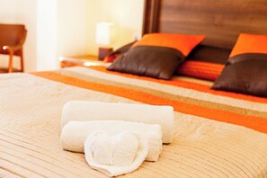 Una cama bien hecha con una colcha a rayas, una toalla blanca enrollada y dos almohadas.