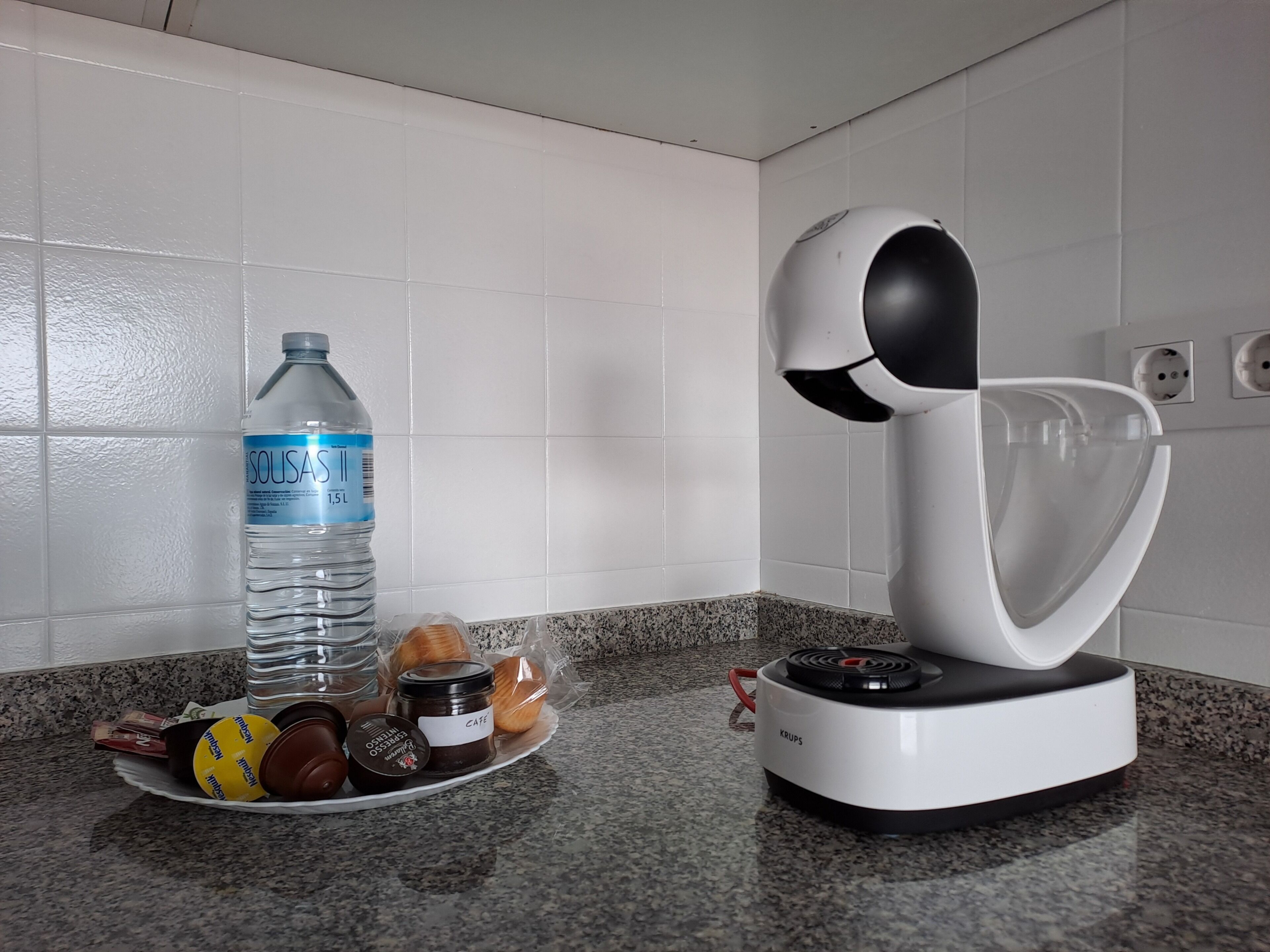 A kitchen with a water bottle, a plate with food items, and a coffee machine.
