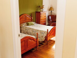 Un dormitorio con dos camas de madera, un aparador, una silla y una lámpara.