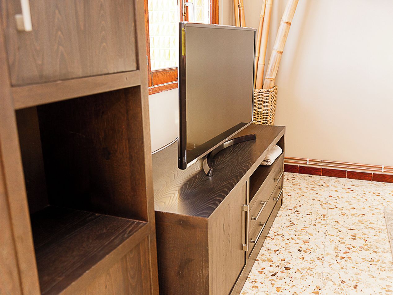 Un mueble de madera con un televisor de pantalla plana encima, una cesta tejida y un suelo de baldosas.