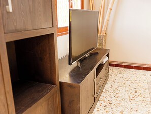 Un mueble de madera con un televisor de pantalla plana encima, una cesta tejida y un suelo de baldosas.