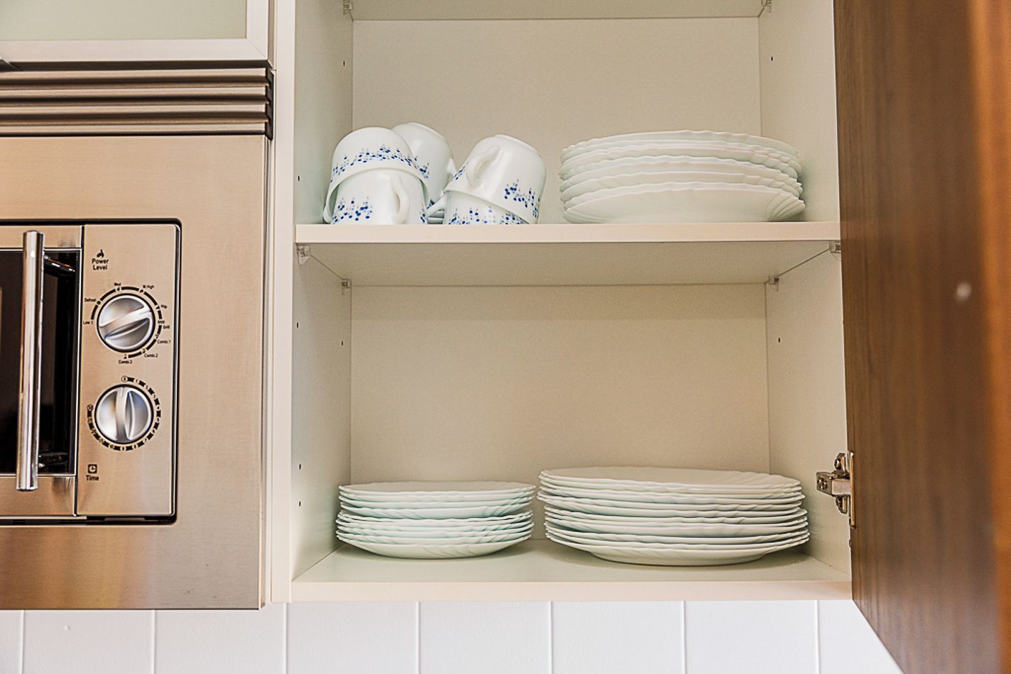 Una cocina con horno tostador integrado y estantes con platos y tazas.