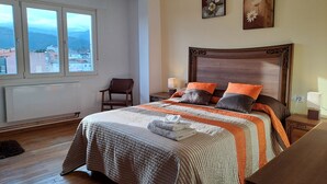 A bedroom with a large bed, a chair, a view of the city through the window, and a decorative ceiling light. - Torre Plaza 5. A spacious apartment in Boiro, beaches and terraces. (BOIRO)