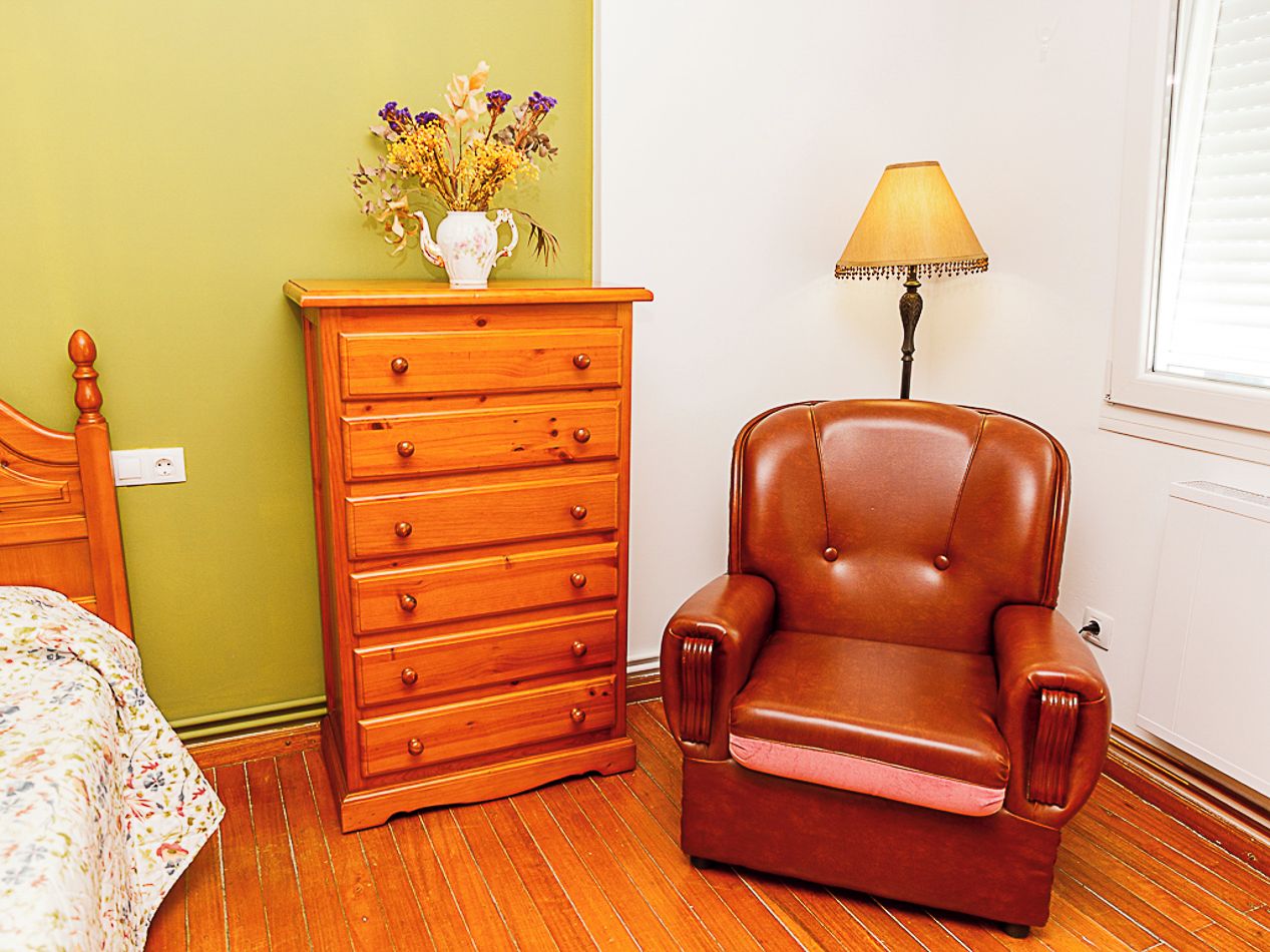 Una habitación con un aparador de madera, un sillón de cuero, una lámpara y una cama con ropa de cama floral.