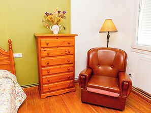 Une pièce comprenant une commode en bois, un fauteuil en cuir, une lampe et un lit avec une literie à motifs floraux.