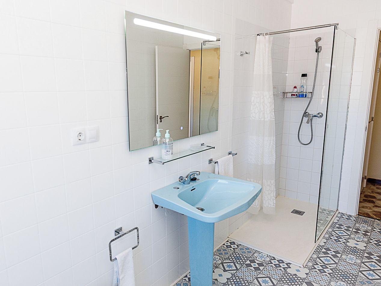 Un baño con un lavamanos azul, cabina de ducha de vidrio y suelo estampado.