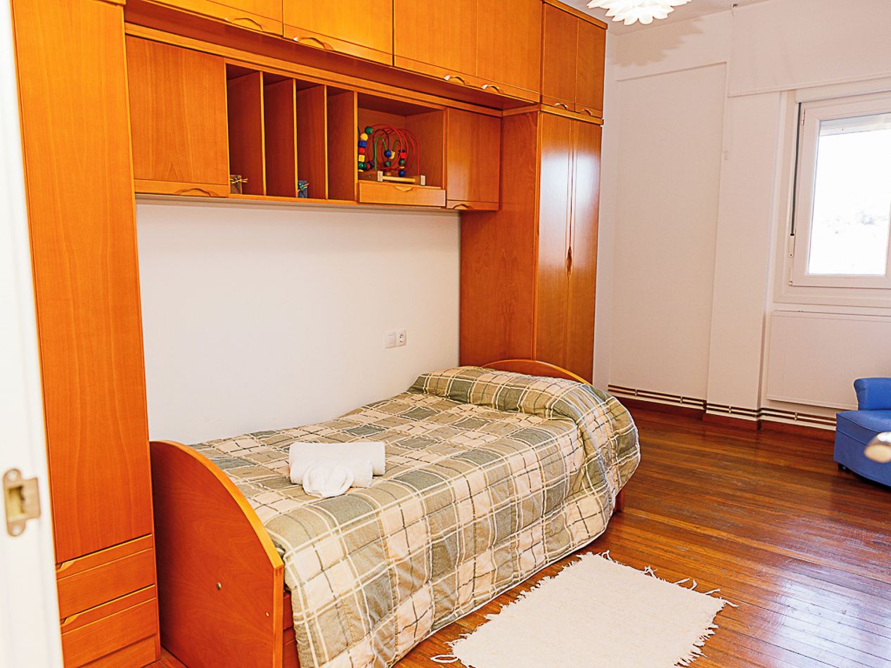 A compact bedroom with a single bed, wooden wardrobe, and a small window.