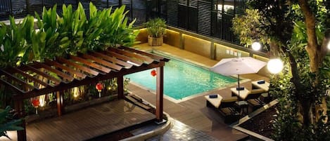 A rooftop pool area with a wooden pergola, lounge chairs, and potted plants.