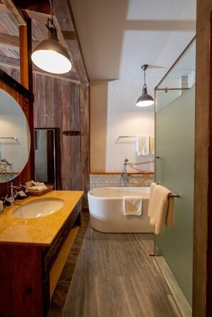 Une salle de bain avec un meuble-lavabo en bois, un grand miroir, une baignoire et un espace douche.