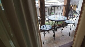 Un balcon avec une table ronde et quatre chaises, agrémenté d’une nappe à motifs et de rampes en métal.