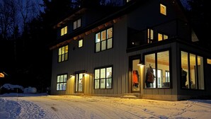 Moderni, kaksikerroksinen rakennus, jossa on suuret ikkunat ja parveke, ja sen ympärillä on lunta.